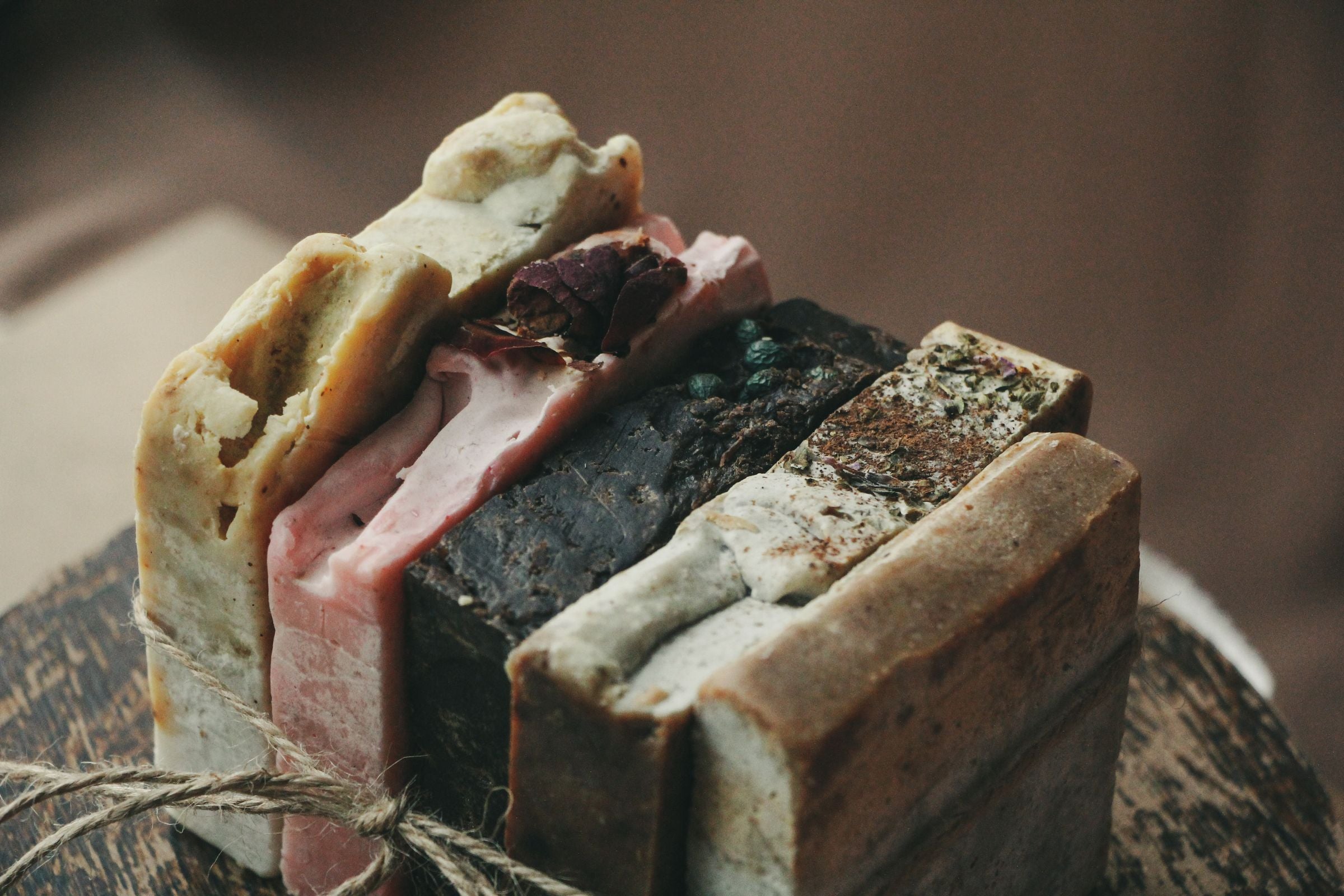 Stack of rustic handmade soap bars tied with twine on a wooden surface